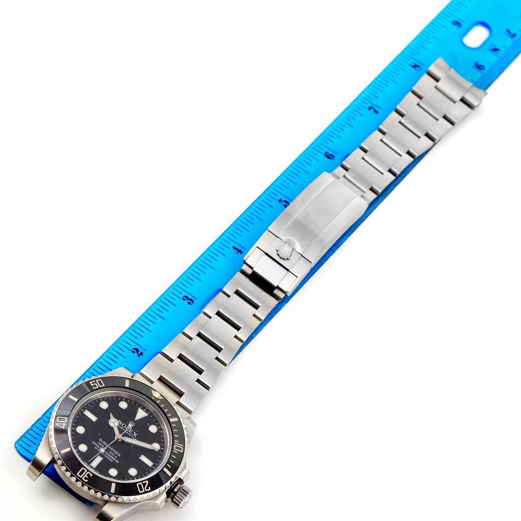 The Rolex Submariner 114060 Men's Stainless Steel Black Dial 114060 Men's Stainless Steel Black Dial watch is shown from an overhead angle, displaying the dial, bezel, bracelet, and clasp next to a ruler for scale.