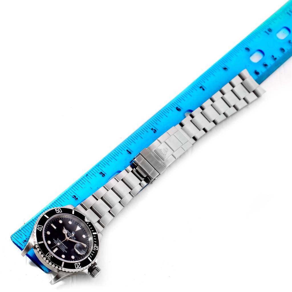 The Rolex Submariner 16610 Men's Stainless Steel Black Dial 16610 Men's Stainless Steel Black Dial watch is shown in a top-down angle, displaying its dial, bezel, and metal bracelet alongside a ruler.