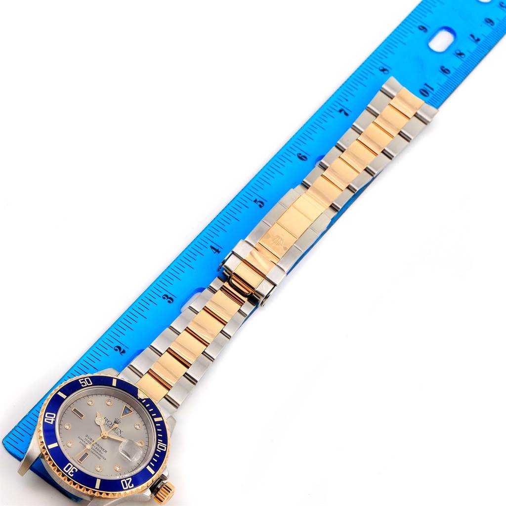 The Rolex Submariner 16613 Men's Steel and Gold (two tone) Grey Dial 16613 Men's Steel and Gold (two tone) Grey Dial watch is shown from a top-down angle, displaying the face and bracelet alongside a ruler for measurement.