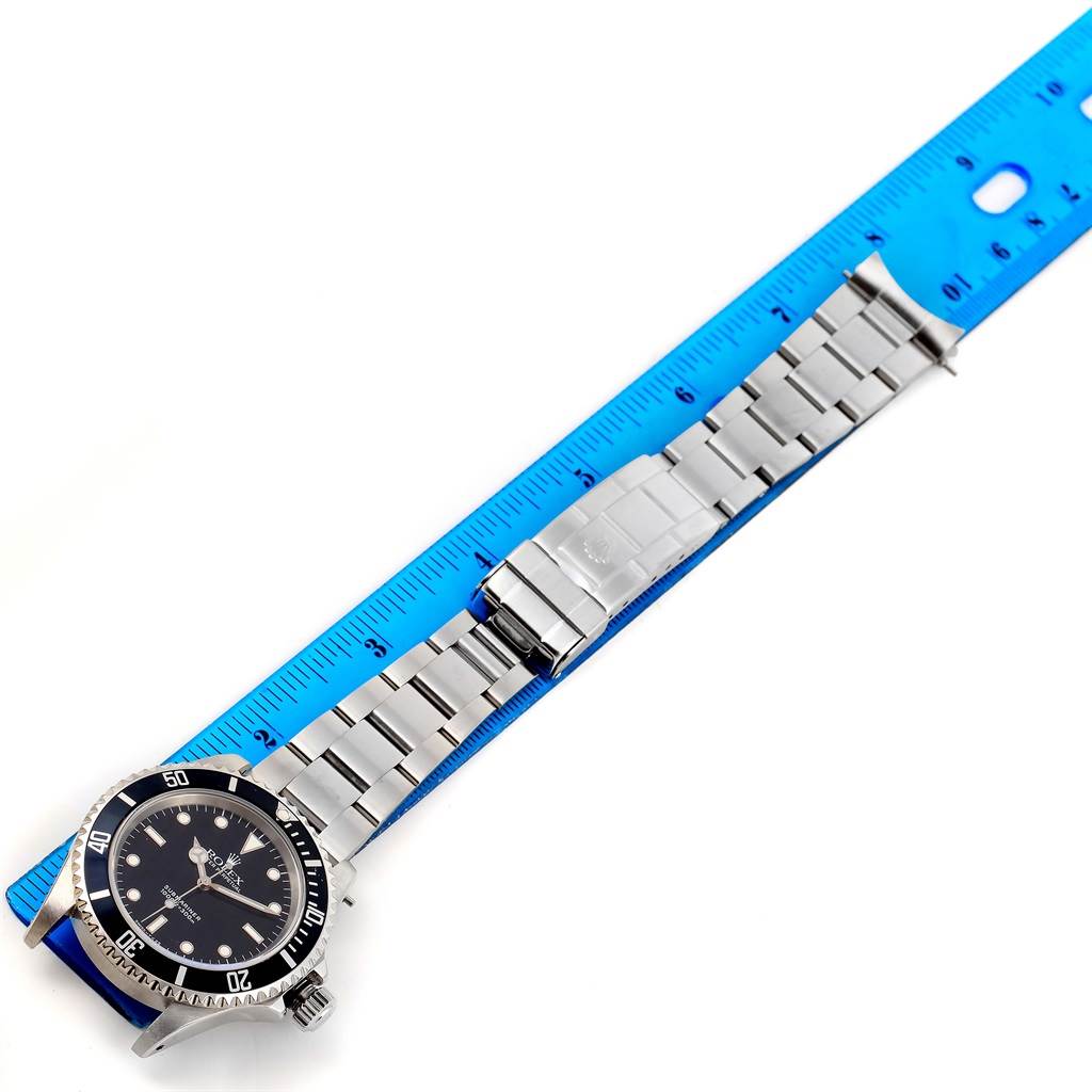 The image shows a Rolex Submariner 14060 Men's Stainless Steel Black Dial 14060 Men's Stainless Steel Black Dial watch lying flat against a blue ruler, displaying the face, bracelet, and clasp.