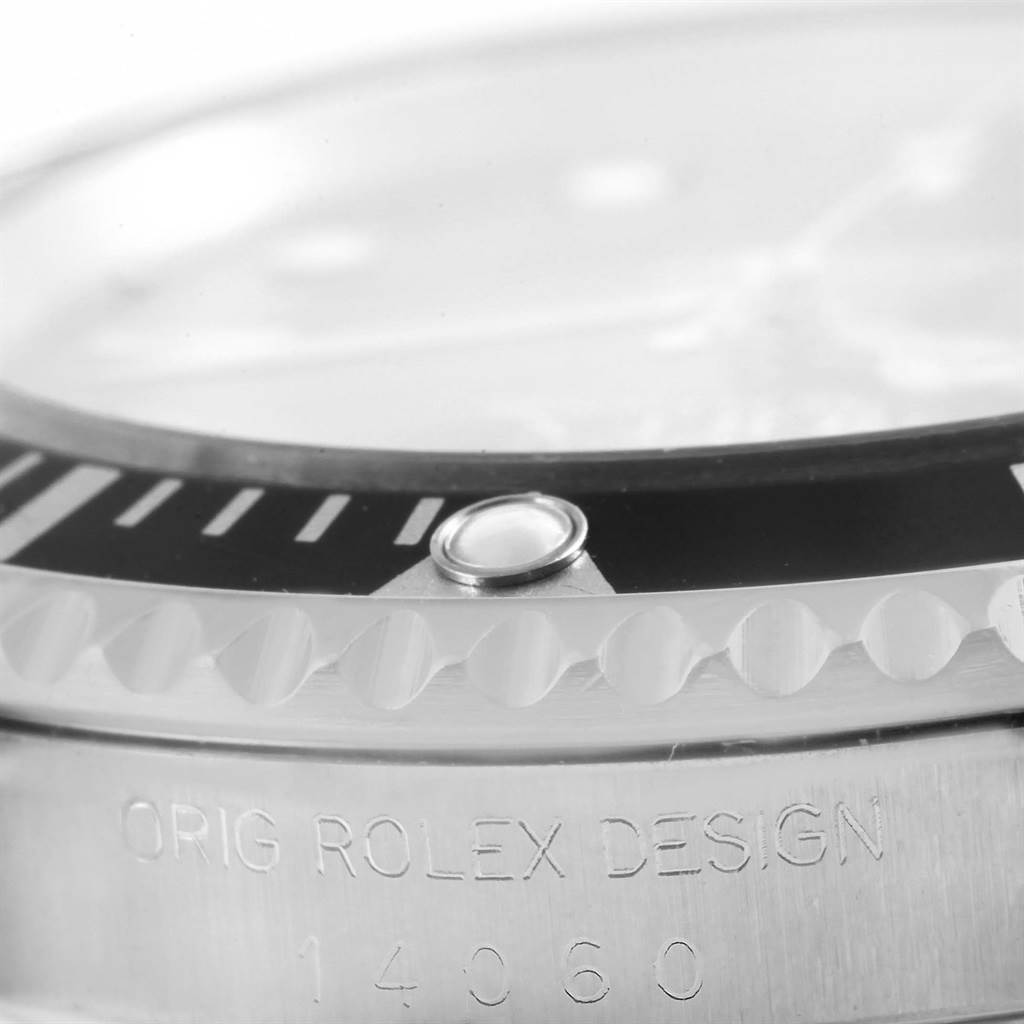 This close-up image of a Rolex Submariner 14060 Men's Stainless Steel Black Dial 14060 Men's Stainless Steel Black Dial shows the watch bezel, the luminous pip, and part of the case with the engraved design number.