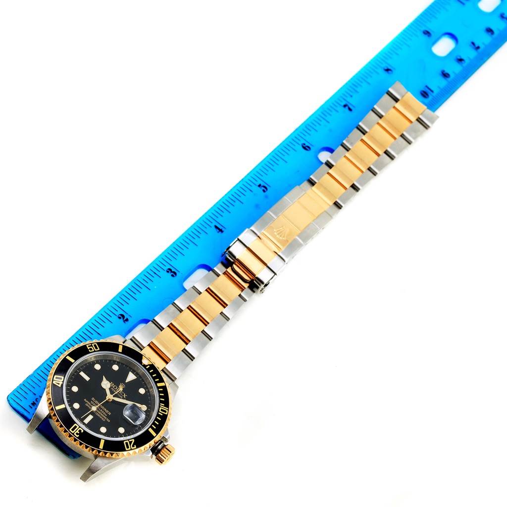 The image shows a Rolex Submariner 16613 Men's Steel and Gold (two tone) Black Dial 16613 Men's Steel and Gold (two tone) Black Dial watch laid flat with a measuring ruler to its side.