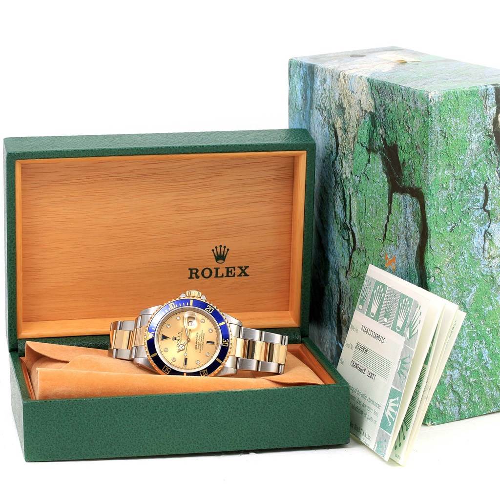 The image shows a Rolex Submariner 16613 Men's Steel and Gold (two tone) Champagne Dial 16613 Men's Steel and Gold (two tone) Champagne Dial watch inside an open green box along with a booklet and the box cover.