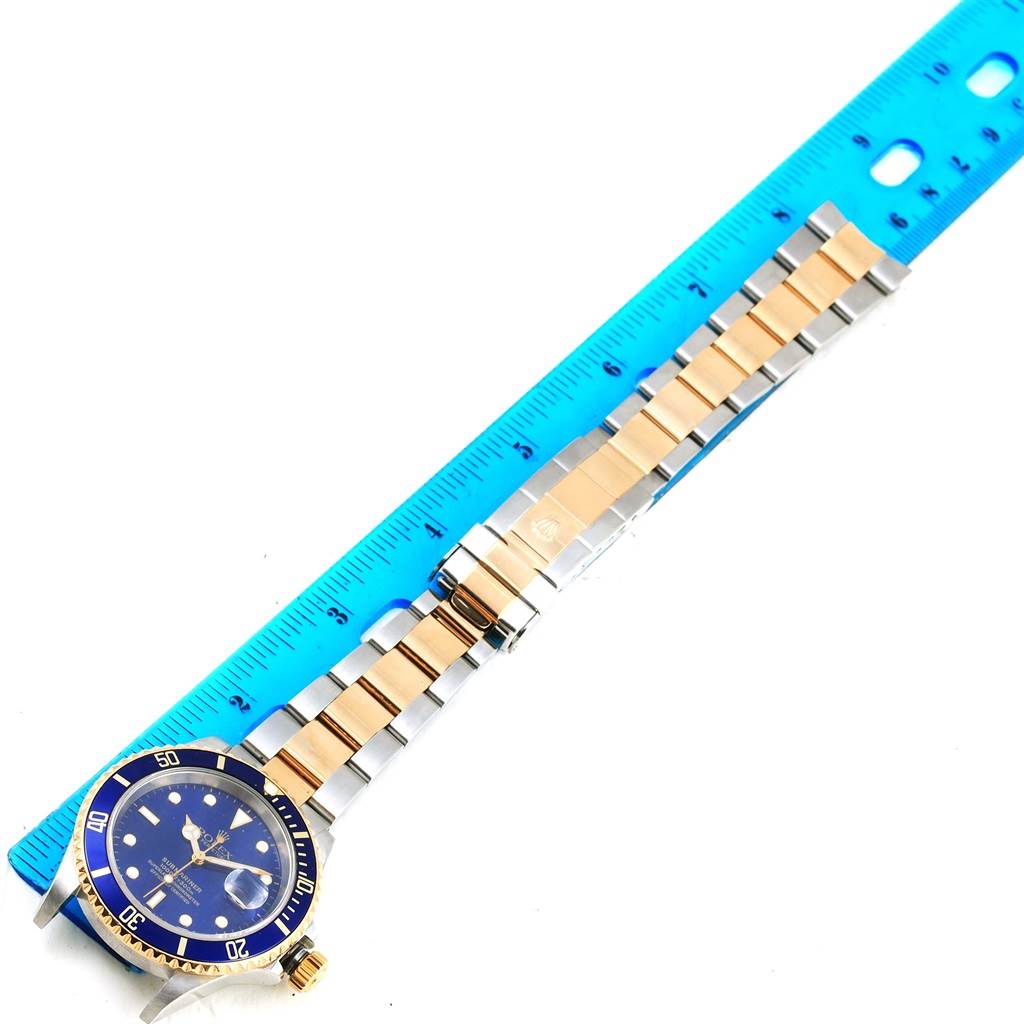 This image shows a Rolex Submariner 16613 Men's Steel and Gold (two tone) Blue Dial 16613 Men's Steel and Gold (two tone) Blue Dial watch laid flat next to a ruler, highlighting the bracelet and face.