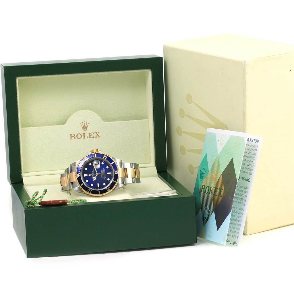 The image shows a Rolex Submariner 16613 Men's Steel and Gold (two tone) Blue Dial 16613 Men's Steel and Gold (two tone) Blue Dial watch in its open box, with the watch, warranty card, and green tag visible.