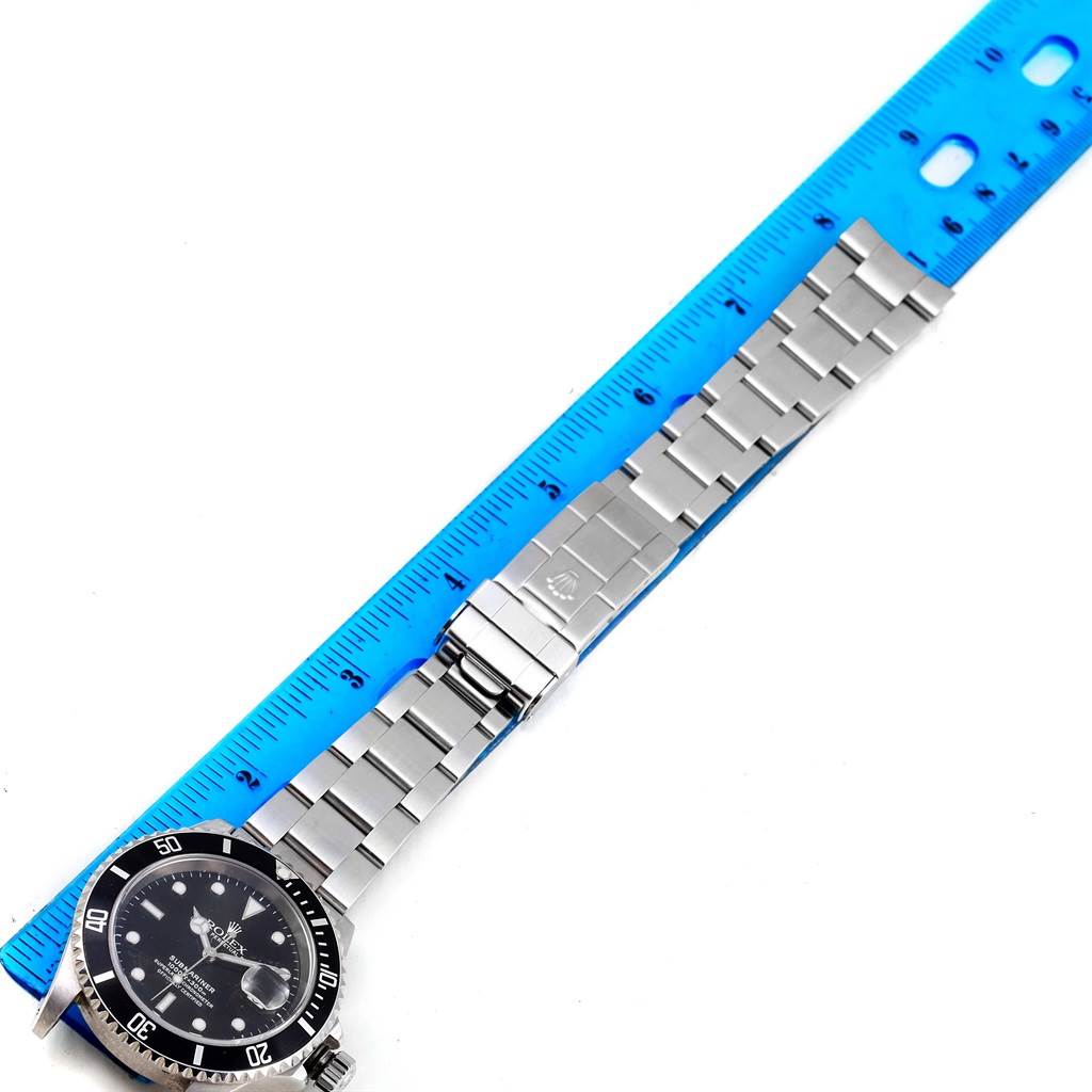 This image shows a Rolex Submariner 16610 Men's Stainless Steel Black Dial 16610 Men's Stainless Steel Black Dial watch laid flat next to a ruler, highlighting its stainless steel bracelet and clasp.