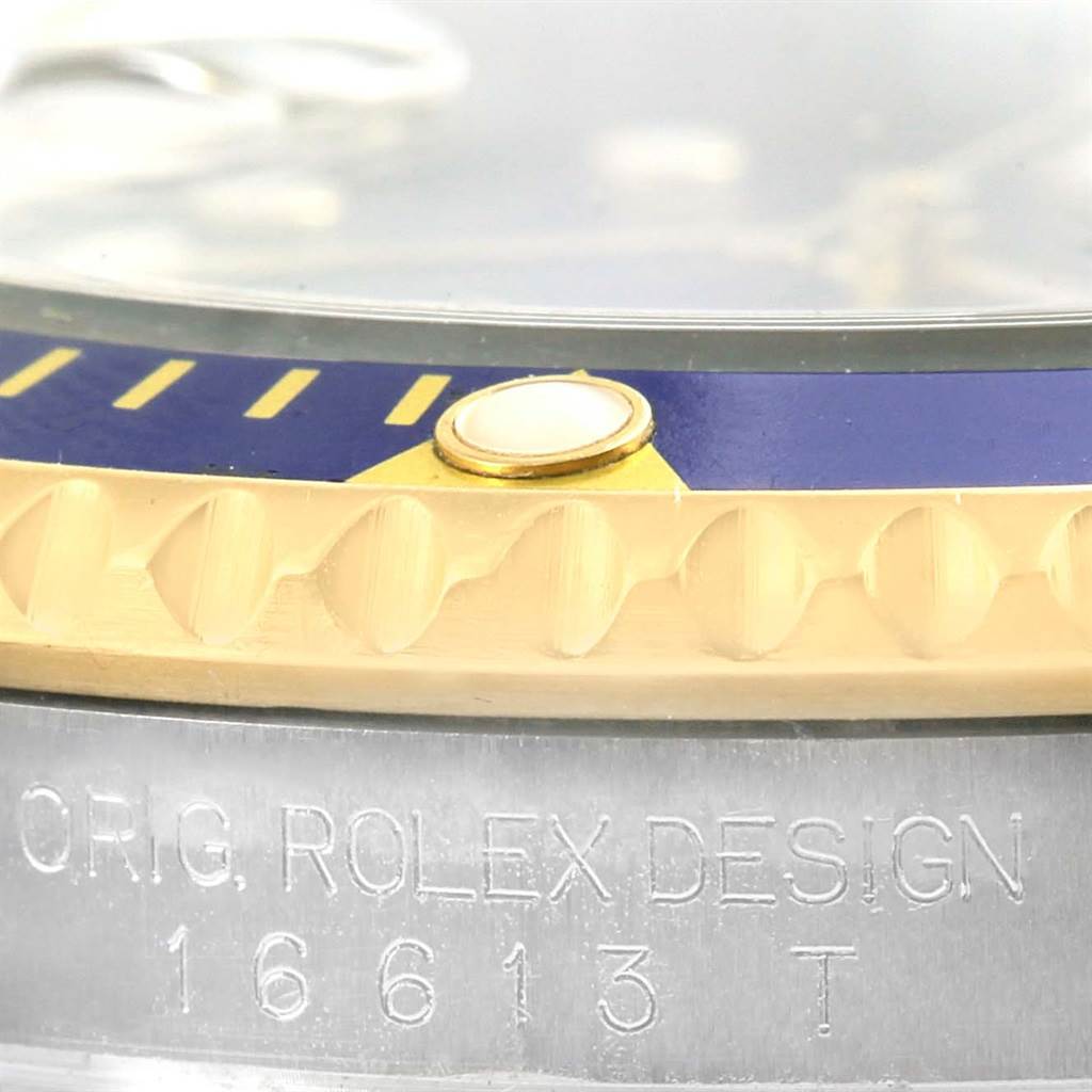This close-up image of the Rolex Submariner 16613 Men
s Steel and Gold (two tone) Blue Dial 16613 Men
s Steel and Gold (two tone) Blue Dial watch shows the bezel, a portion of the crystal, and part of the casing with the model number 16613.