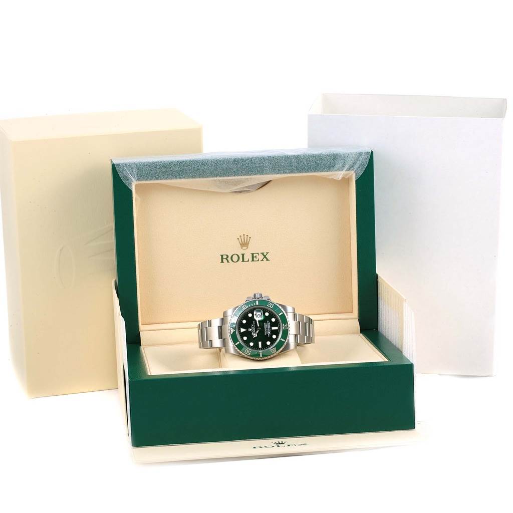 The photo shows a Rolex Submariner 116610LV Men
s Stainless Steel Green Dial 116610LV Men
s Stainless Steel Green Dial watch inside its green and beige branded box, with additional packaging visible.