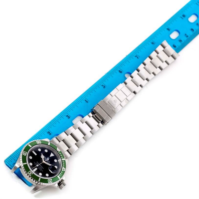 This image shows the top view of a Rolex Submariner 16610LV Men
s Stainless Steel Black Dial 16610LV Men
s Stainless Steel Black Dial watch with its metal bracelet next to a blue ruler for scale.