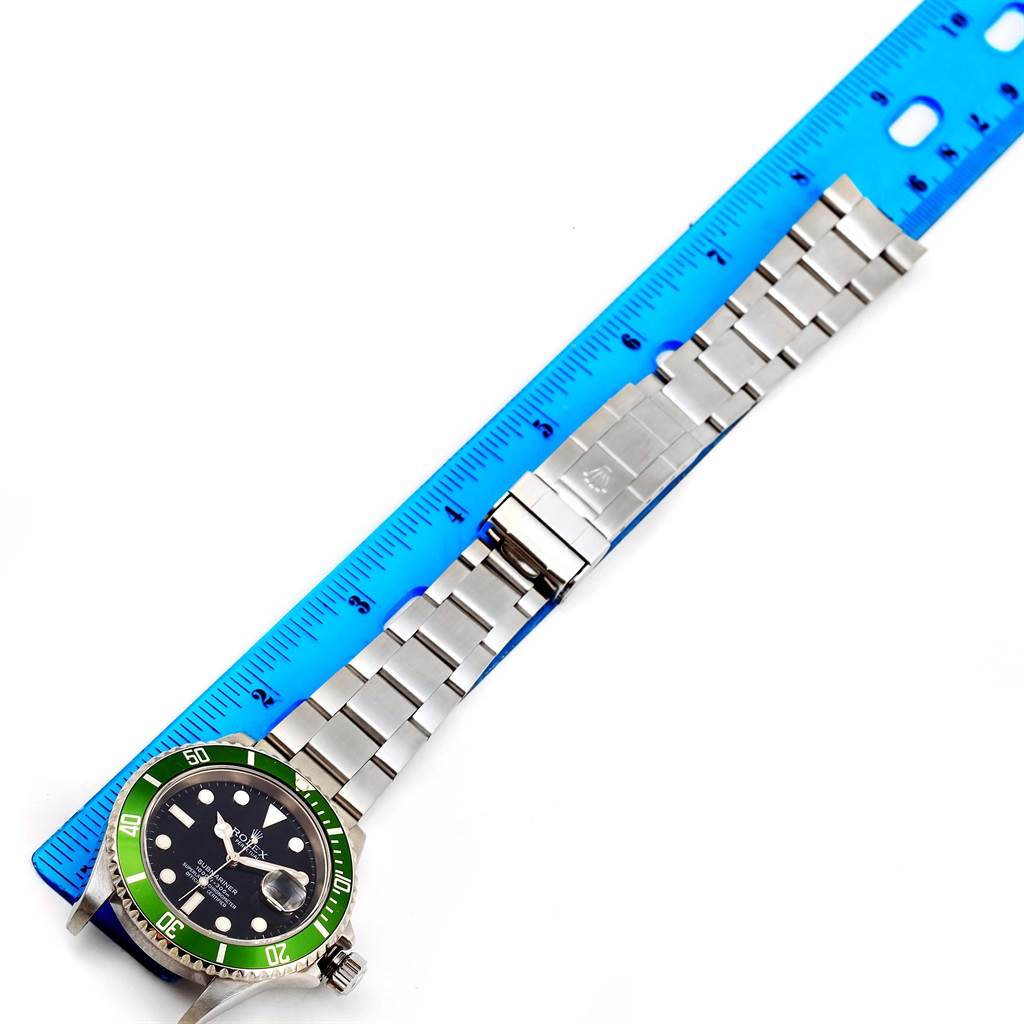 The image shows a Rolex Submariner 16610LV Men
s Stainless Steel Black Dial 16610LV Men
s Stainless Steel Black Dial watch laid flat, with its face, bracelet, and clasp visible, next to a ruler for scaling.