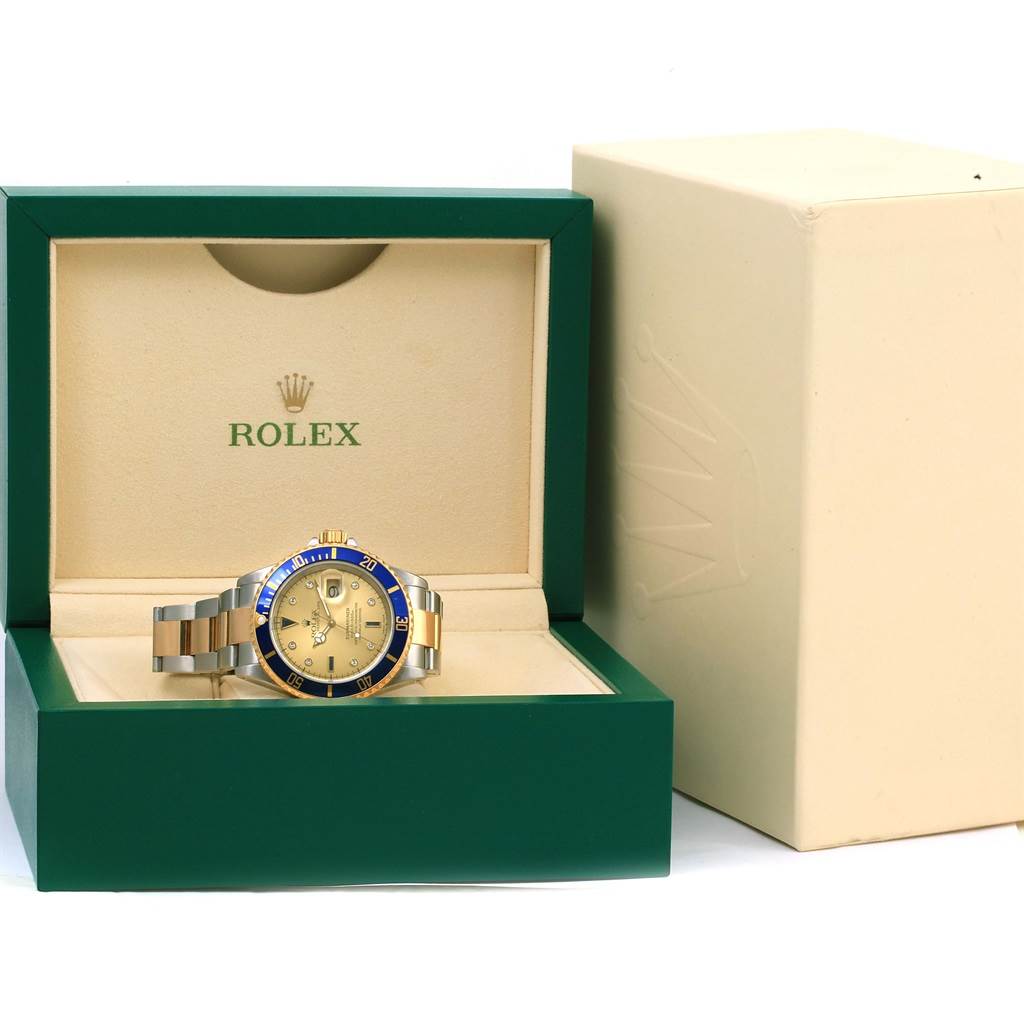 The image shows a Rolex Submariner 16613 Men
s Steel and Gold (two tone) Champagne Dial 16613 Men
s Steel and Gold (two tone) Champagne Dial watch from the front, placed inside its green and beige box, with the outer box nearby.