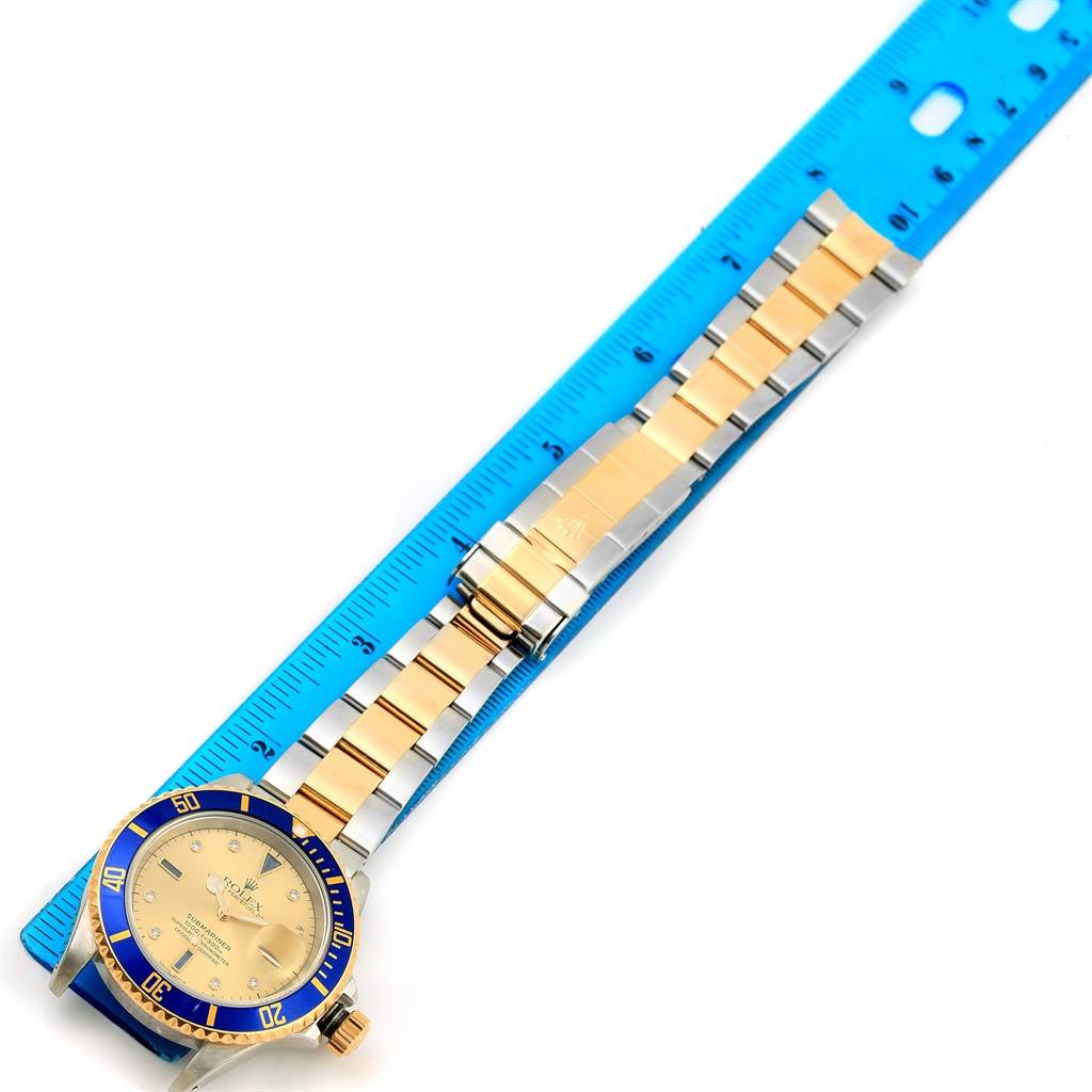 The image shows a top-down view of the Rolex Submariner 16613 Men
s Steel and Gold (two tone) Champagne Dial 16613 Men
s Steel and Gold (two tone) Champagne Dial watch, including its face, bezel, and two-tone bracelet strap next to a blue ruler.