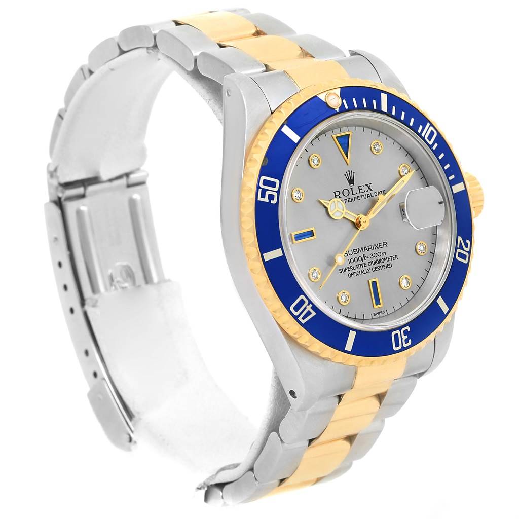 The image shows a Rolex Submariner 16613 Men
s Steel and Gold (two tone) Grey Dial 16613 Men
s Steel and Gold (two tone) Grey Dial watch at an oblique angle, highlighting its two-tone bracelet, blue bezel, and silver dial.
