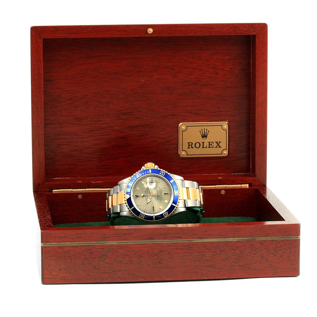 The Rolex Submariner 16613 Men
s Steel and Gold (two tone) Grey Dial 16613 Men
s Steel and Gold (two tone) Grey Dial is displayed front-facing in an open wooden box with a brass Rolex logo plaque.