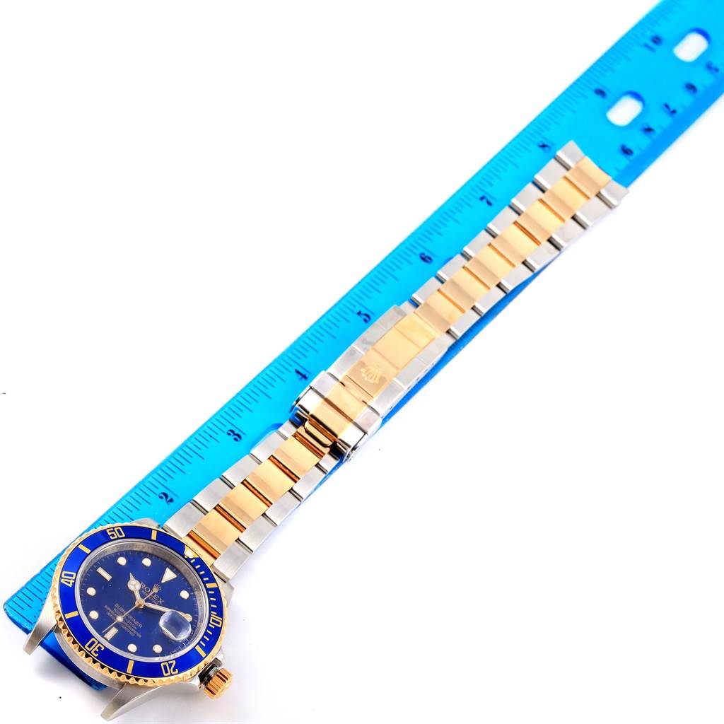 The image shows the full length of the Rolex Submariner 16613 Men
s Steel and Gold (two tone) Blue Dial 16613 Men
s Steel and Gold (two tone) Blue Dial watch, including the dial, bezel, and bracelet, with a blue ruler for scale.