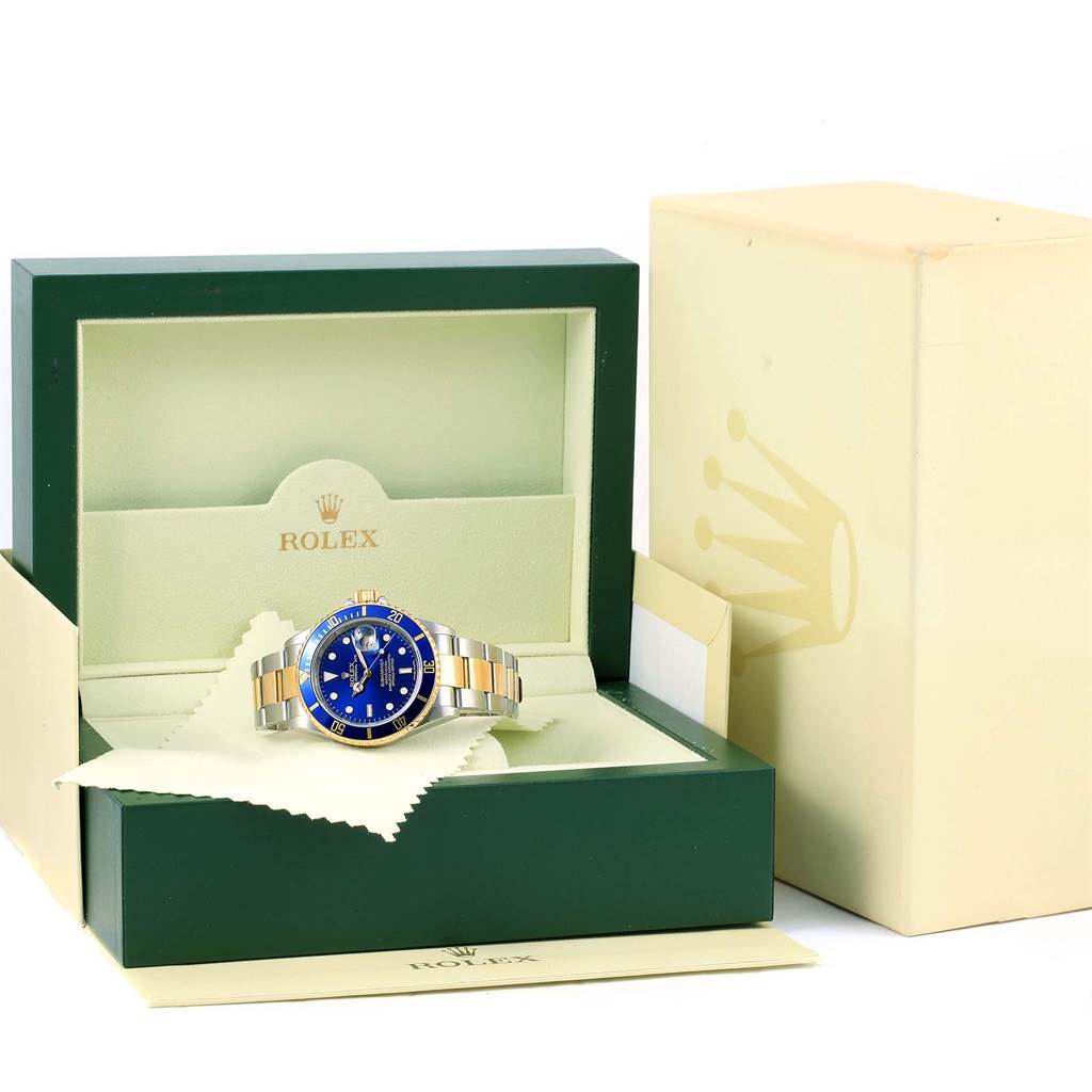 The Rolex Submariner 16613 Men
s Steel and Gold (two tone) Blue Dial 16613 Men
s Steel and Gold (two tone) Blue Dial watch is shown inside its green watch box with the lid open, alongside a beige outer box.