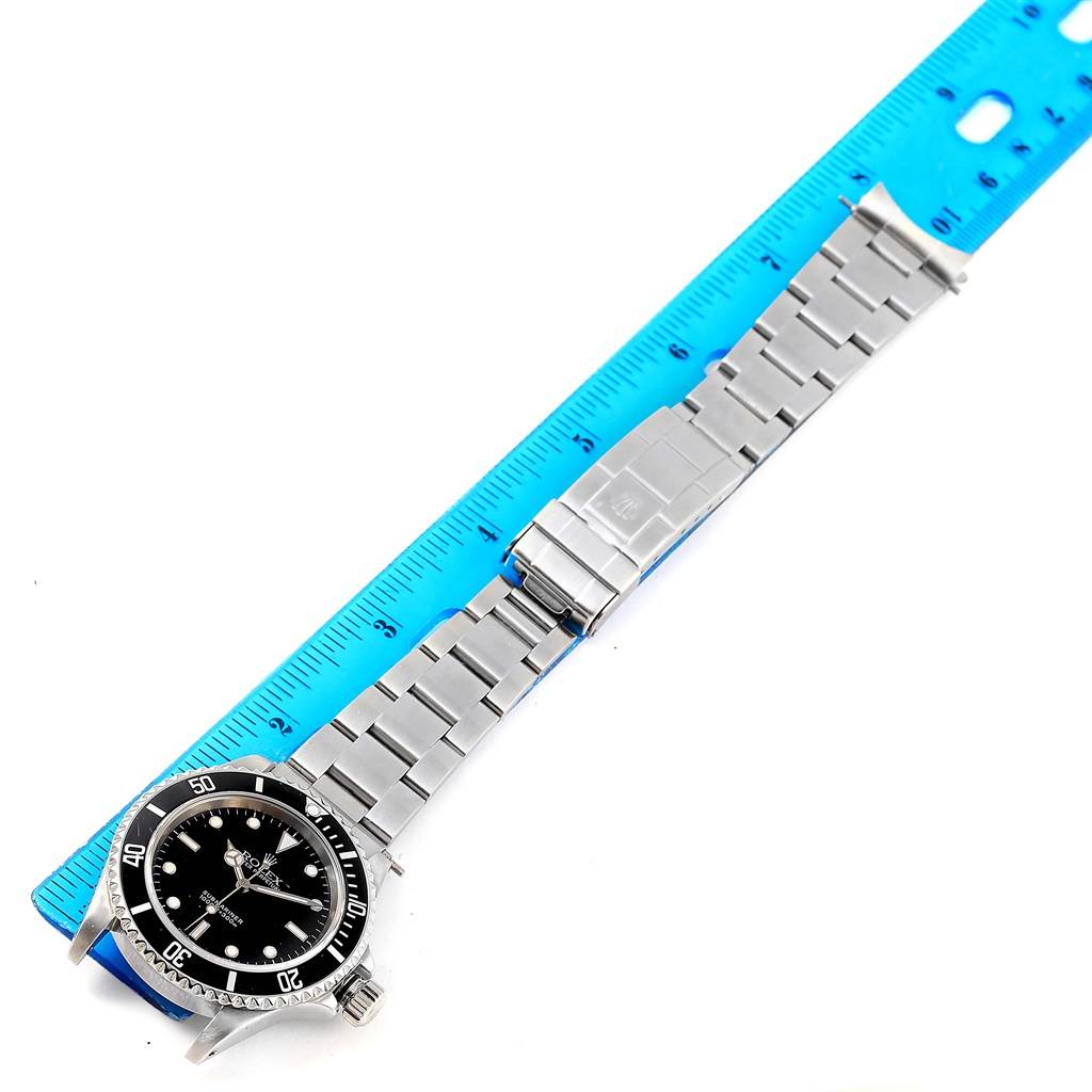 The image shows a top view of a Rolex Submariner 14060 Men
s Stainless Steel Black Dial 14060 Men
s Stainless Steel Black Dial watch, highlighting the face, bezel, bracelet, and clasp against a ruler for scale.