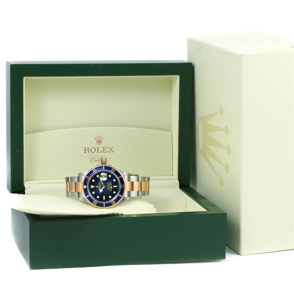 The Rolex Submariner 16613 Men
s Steel and Gold (two tone) Blue Dial 16613 Men
s Steel and Gold (two tone) Blue Dial watch is displayed frontally in an open green box with a beige interior; the outer box is to the right.