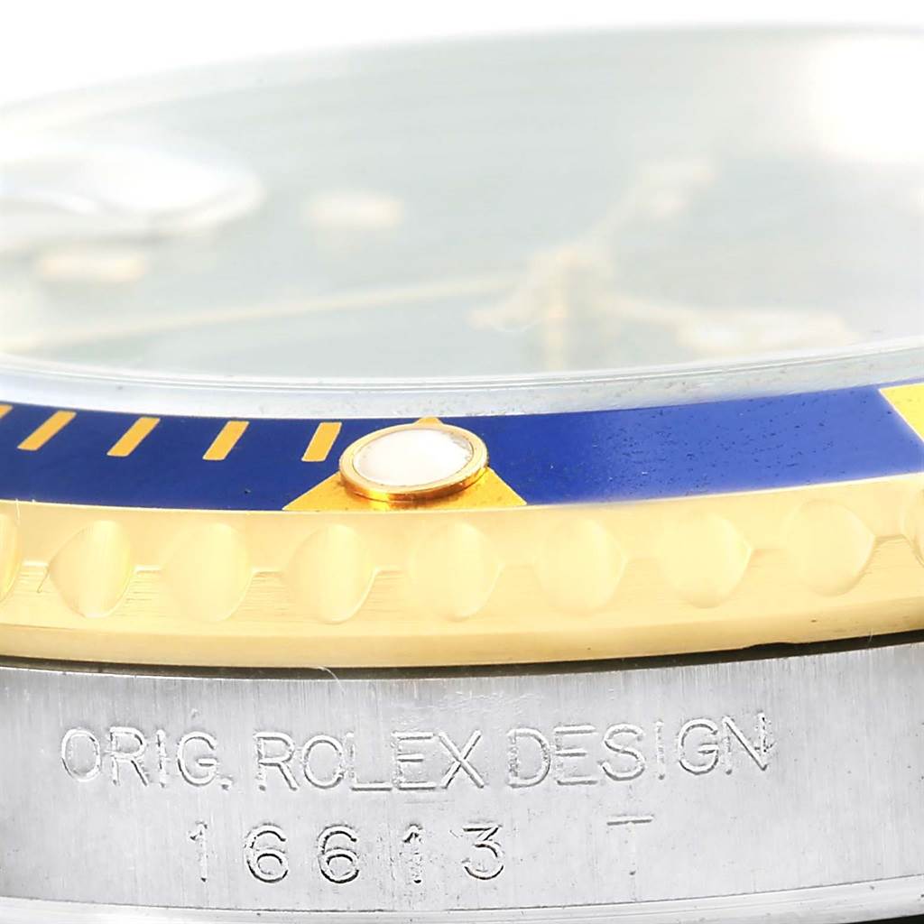 The image shows a close-up view of a Rolex Submariner 16613 Men
s Steel and Gold (two tone) Blue Dial 16613 Men
s Steel and Gold (two tone) Blue Dial
s bezel and case, including the model number engraving.