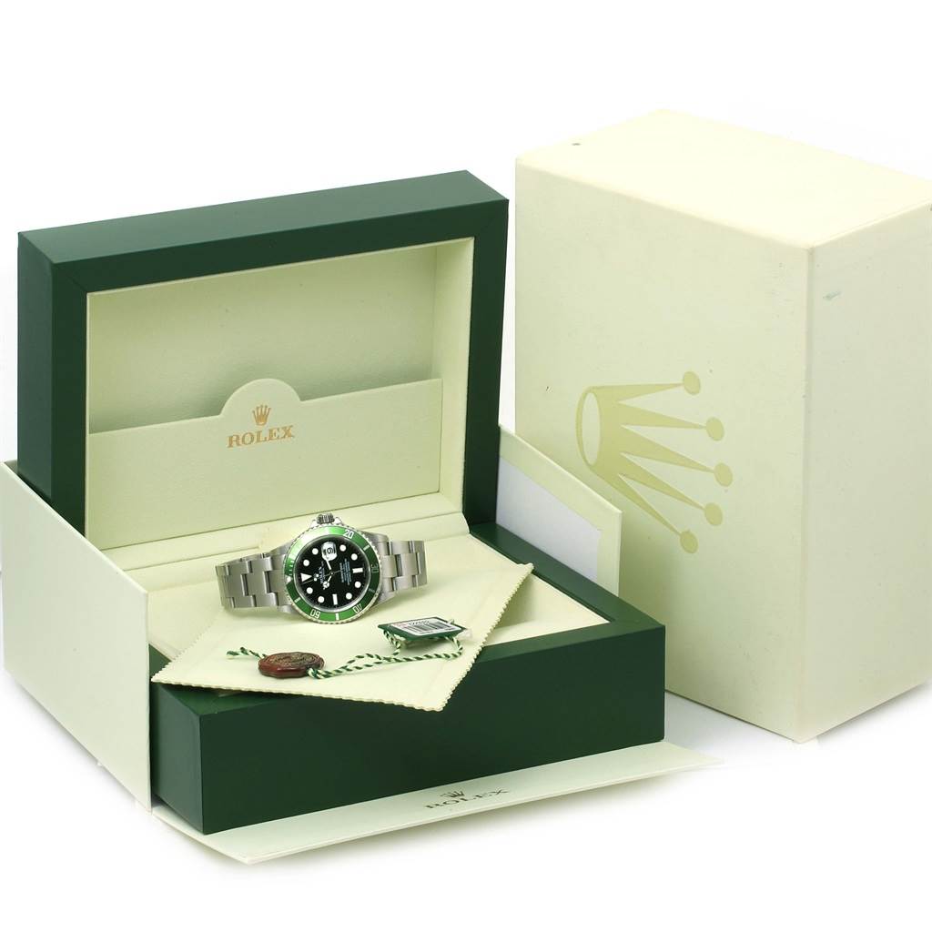 The image shows a Rolex Submariner 16610LV Men
s Stainless Steel Black Dial 16610LV Men
s Stainless Steel Black Dial watch placed inside its open green and cream box along with various accessories.