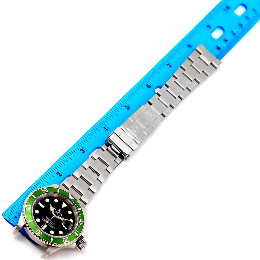 The image shows a top view of a Rolex Submariner 16610LV Men
s Stainless Steel Black Dial 16610LV Men
s Stainless Steel Black Dial watch with a stainless steel bracelet next to a blue ruler for measurement.