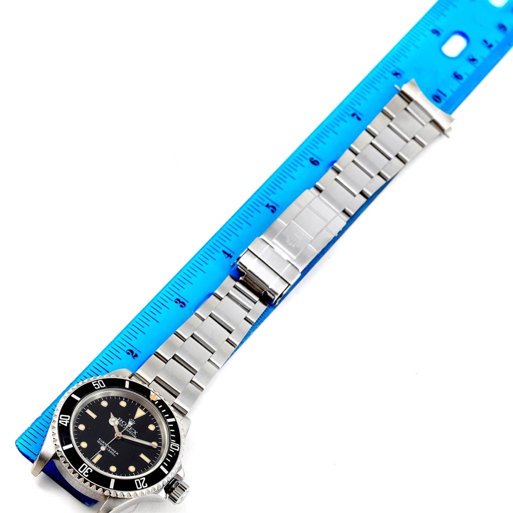 The image shows a Rolex Submariner 14060 Men
s Stainless Steel Black Dial 14060 Men
s Stainless Steel Black Dial watch laid flat with its face and stainless steel bracelet, positioned alongside a ruler.