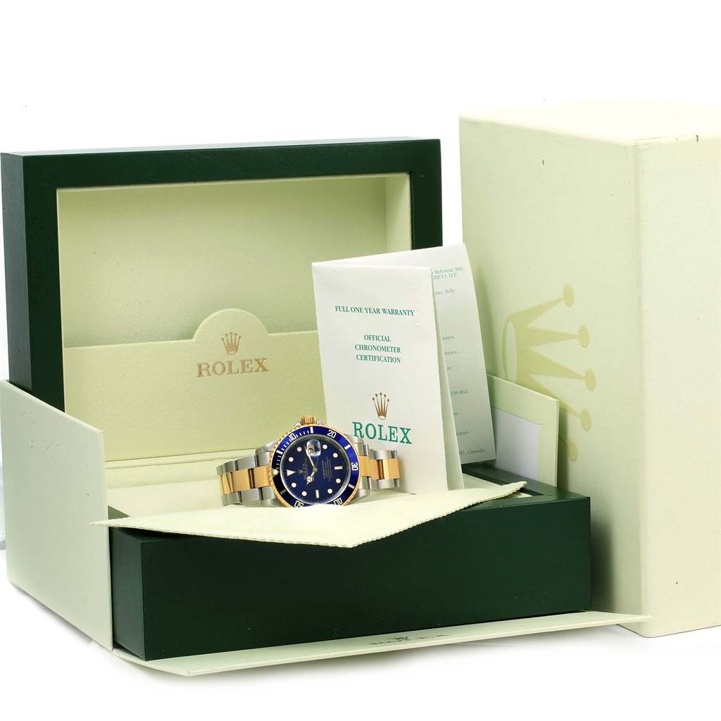 The image shows a Rolex Submariner 16613 Men
s Steel and Gold (two tone) Blue Dial 16613 Men
s Steel and Gold (two tone) Blue Dial watch placed in its open display box alongside warranty cards and documentation from a front angle.