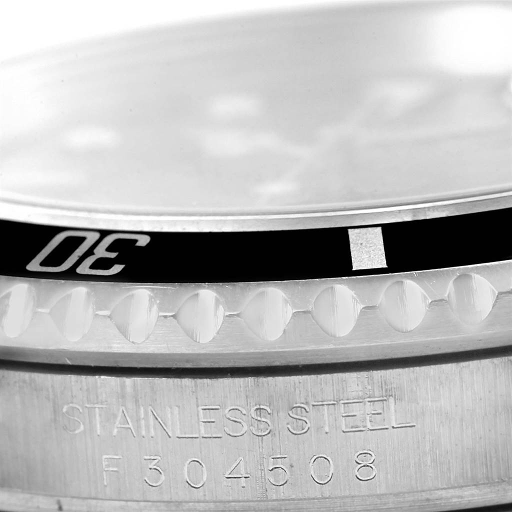 This close-up image of the Rolex Submariner 16610 Men's Stainless Steel Black Dial 16610 Men's Stainless Steel Black Dial shows part of the bezel, the edge of the dial, and the watch case with the stainless steel inscription.