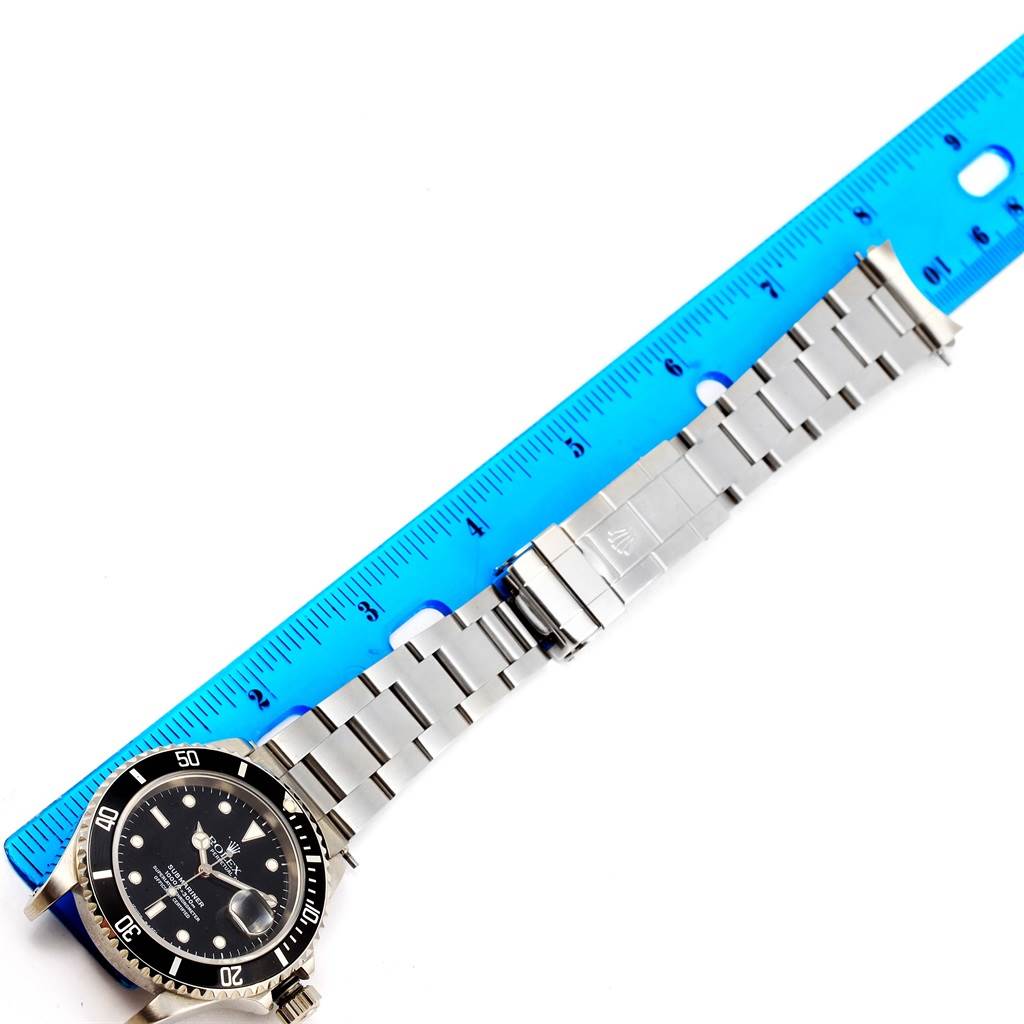 The image shows a top-down angle of a Rolex Submariner 16610 Men
s Stainless Steel Black Dial 16610 Men
s Stainless Steel Black Dial watch and its entire metal bracelet next to a blue ruler.