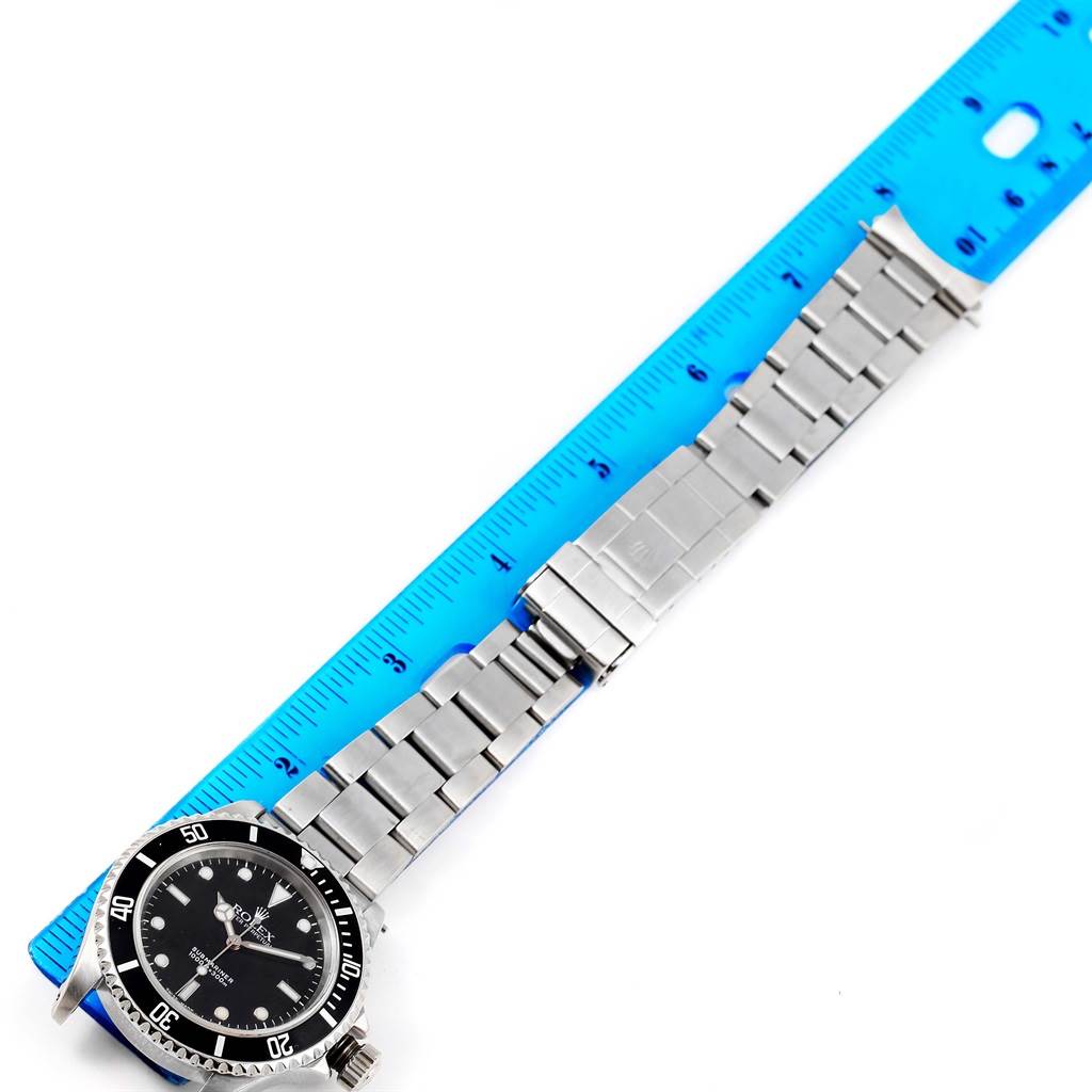 This image shows a Rolex Submariner 14060 Men
s Stainless Steel Black Dial 14060 Men
s Stainless Steel Black Dial watch laid out beside a blue ruler, highlighting the watch
s face, bezel, and bracelet.