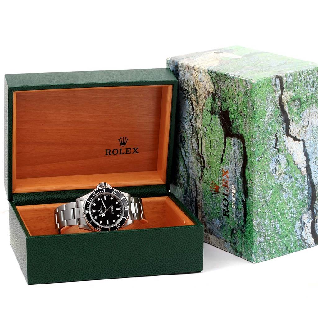 The Rolex Submariner 14060 Men
s Stainless Steel Black Dial 14060 Men
s Stainless Steel Black Dial watch is shown inside its open green and wood display box, with the outer packaging adjacent.