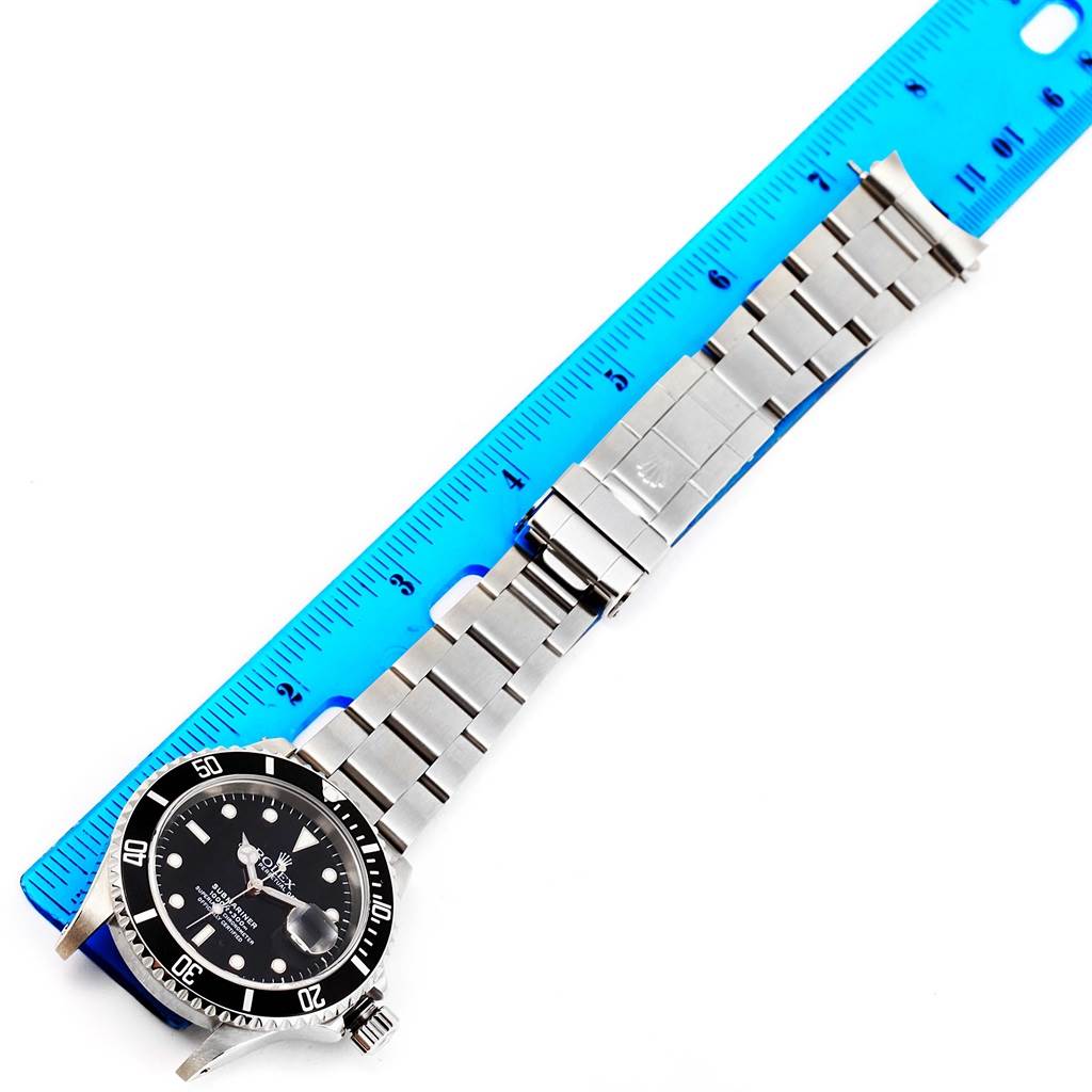 The Rolex Submariner 16610 Men
s Stainless Steel Black Dial 16610 Men
s Stainless Steel Black Dial watch is shown from an overhead angle, featuring its face, bracelet, and clasp next to a blue ruler for scale.