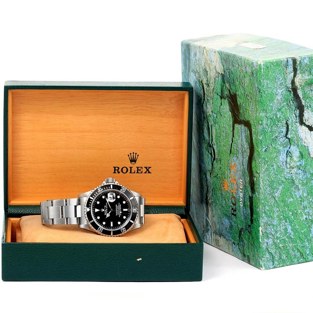 The image shows a Rolex Submariner 16610 Men
s Stainless Steel Black Dial 16610 Men
s Stainless Steel Black Dial watch from a front angle, displayed in an open wooden box, with an additional outer box nearby.