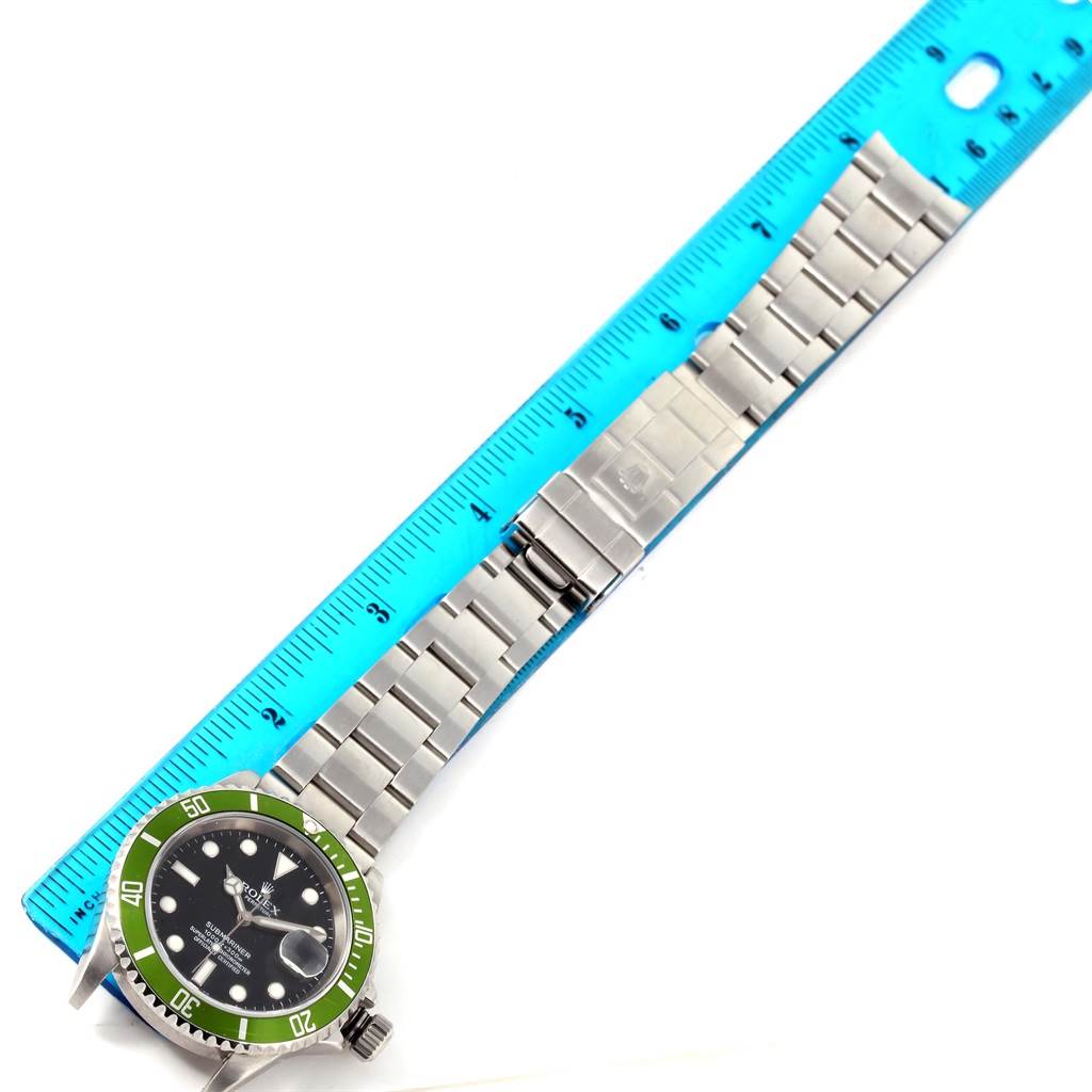 The image shows a top-down view of a Rolex Submariner 16610LV Men
s Stainless Steel Black Dial 16610LV Men
s Stainless Steel Black Dial watch with a green bezel, alongside a blue ruler for size reference.