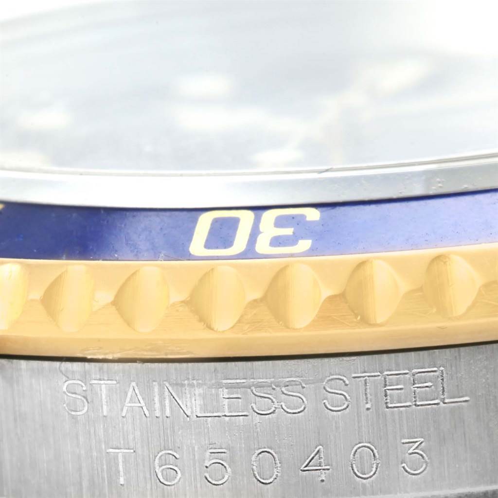 The image shows a close-up of the Rolex Submariner 16613 Men's Steel and Gold (two tone) Blue Dial 16613 Men's Steel and Gold (two tone) Blue Dial's stainless steel case, blue and gold bezel, and part of the serial number engraving.