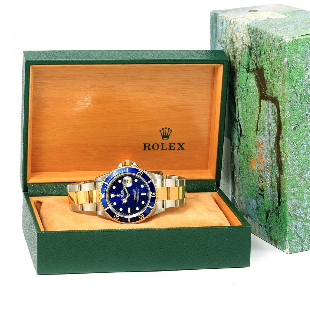 The image shows a front view of a Rolex Submariner 16613 Men's Steel and Gold (two tone) Blue Dial 16613 Men's Steel and Gold (two tone) Blue Dial watch inside its green and wooden Rolex box.