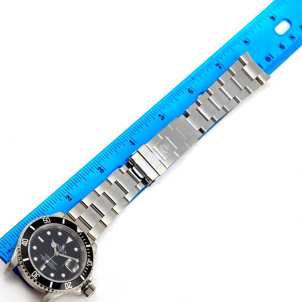 The image shows a top-down angle of a Rolex Submariner 16610 Men
s Stainless Steel Black Dial 16610 Men
s Stainless Steel Black Dial watch with its metal bracelet, aligned next to a blue ruler for scale.