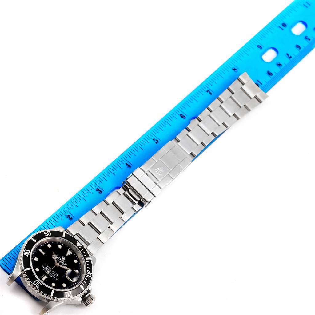 The image shows a top-down view of a Rolex Submariner 16610 Men's Stainless Steel Black Dial 16610 Men's Stainless Steel Black Dial watch, its full metal bracelet, and a blue ruler for scale.