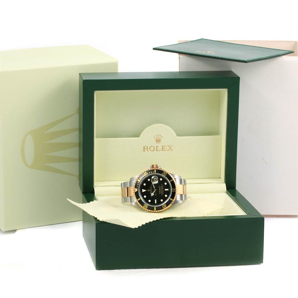 The image shows a Rolex Submariner 16613 Men
s Steel and Gold (two tone) Black Dial 16613 Men
s Steel and Gold (two tone) Black Dial watch positioned inside its green and beige Rolex packaging box with the lid open.