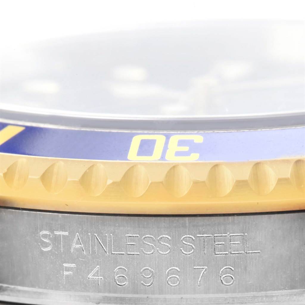 This close-up image of the Rolex Submariner 16613 Men
s Steel and Gold (two tone) Blue Dial 16613 Men
s Steel and Gold (two tone) Blue Dial watch shows the bezel, part of the face, and the stainless steel case with an engraved serial number.