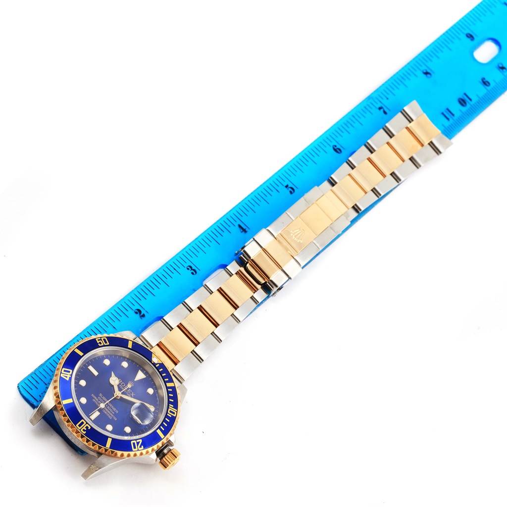 This image shows the full face and bracelet of a Rolex Submariner 16613 Men
s Steel and Gold (two tone) Blue Dial 16613 Men
s Steel and Gold (two tone) Blue Dial watch, laid next to a blue ruler for size reference.