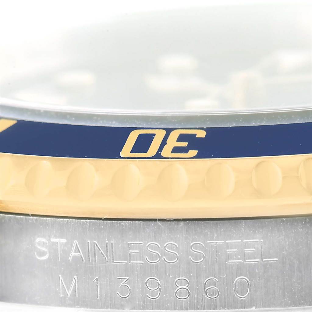 This close-up image of a Rolex Submariner 16613 Men
s Steel and Gold (two tone) Blue Dial 16613 Men
s Steel and Gold (two tone) Blue Dial shows the bezel and part of the case with its engraved model number, M139860.