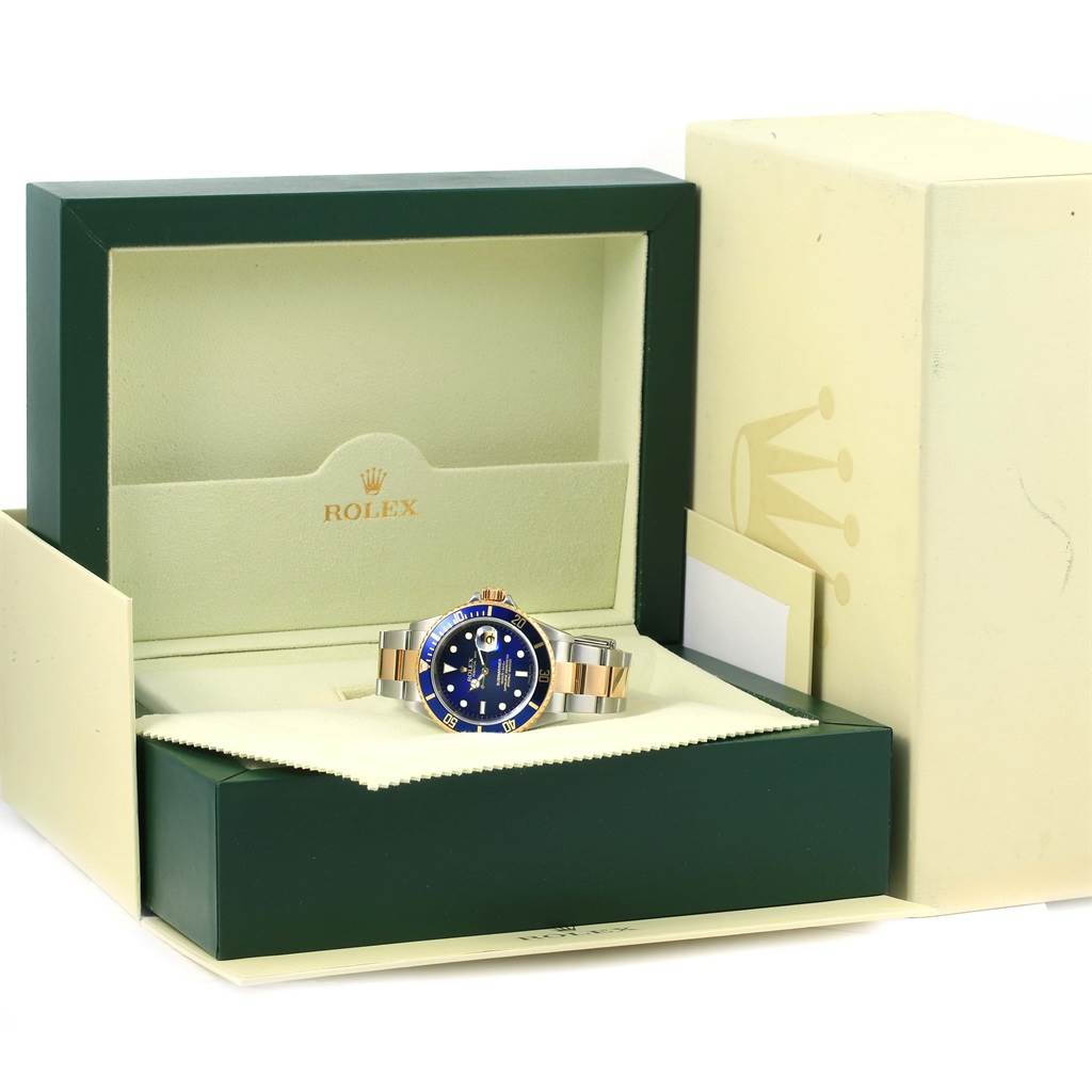 The image shows a Rolex Submariner 16613 Men
s Steel and Gold (two tone) Blue Dial 16613 Men
s Steel and Gold (two tone) Blue Dial watch with a blue dial and bezel, displayed inside its open green and cream-colored box.