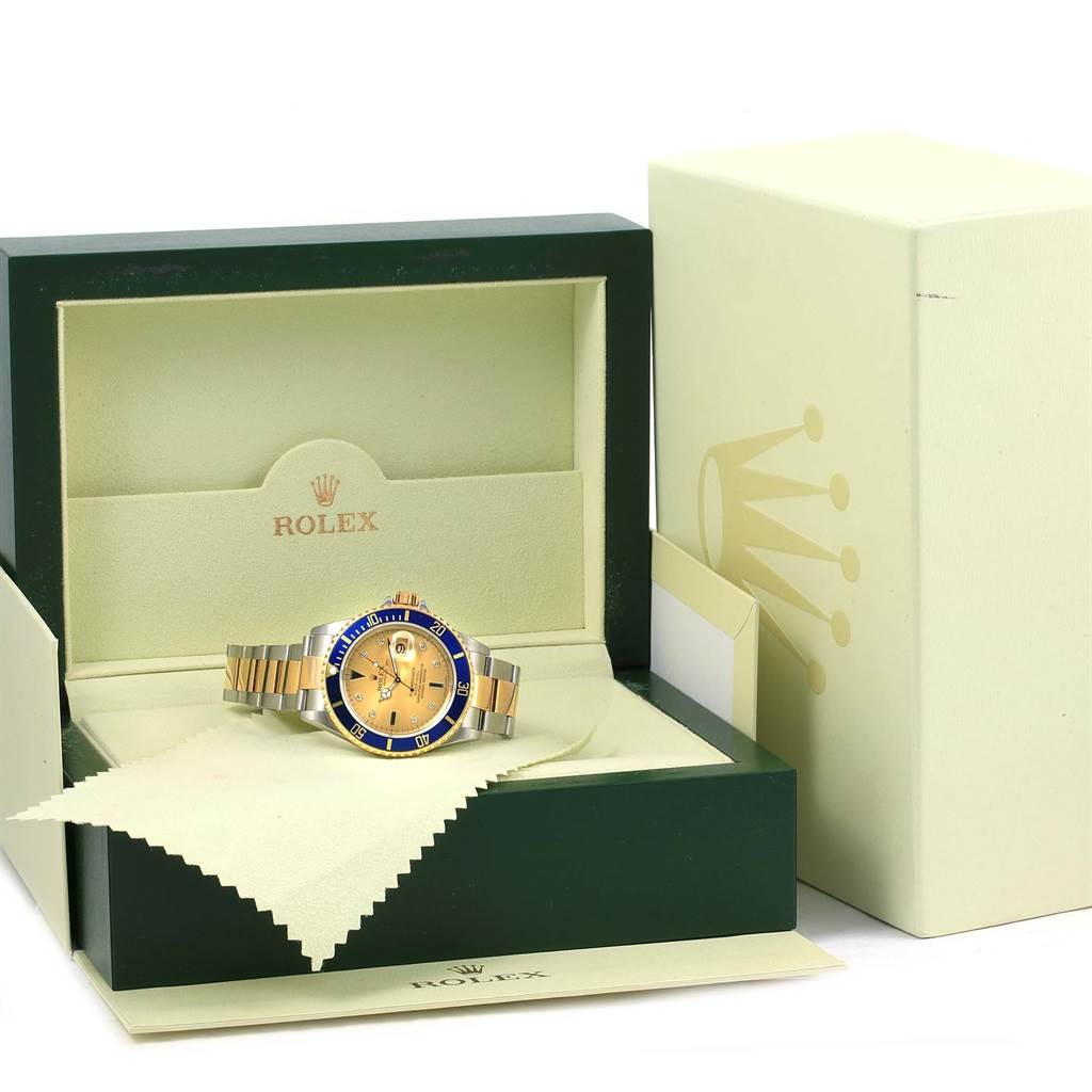 The image shows a Rolex Submariner 16613 Men
s Steel and Gold (two tone) Champagne Dial 16613 Men
s Steel and Gold (two tone) Champagne Dial watch with a blue bezel and gold center dial, displayed in an open green box.