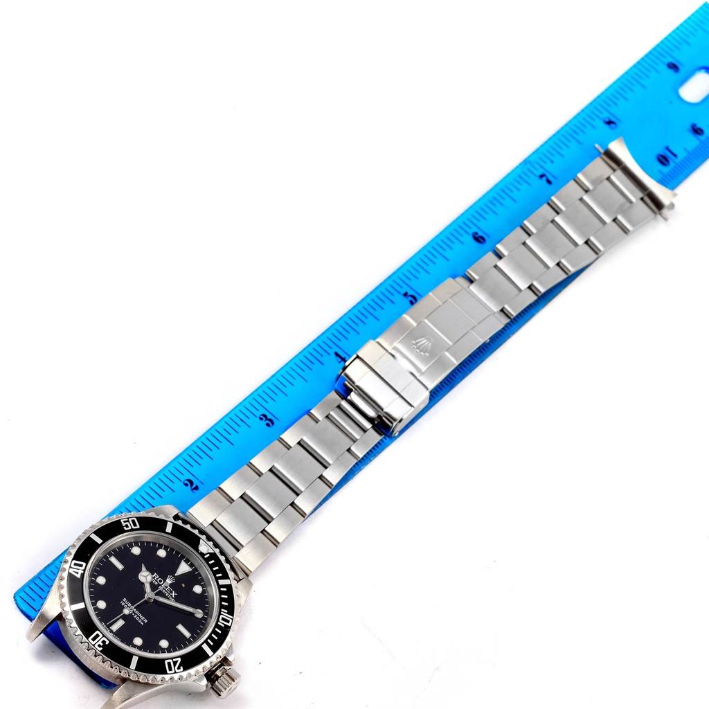 The Rolex Submariner 14060 Men
s Stainless Steel Black Dial 14060 Men
s Stainless Steel Black Dial watch is shown from a top-down angle, fully extended next to a blue ruler.