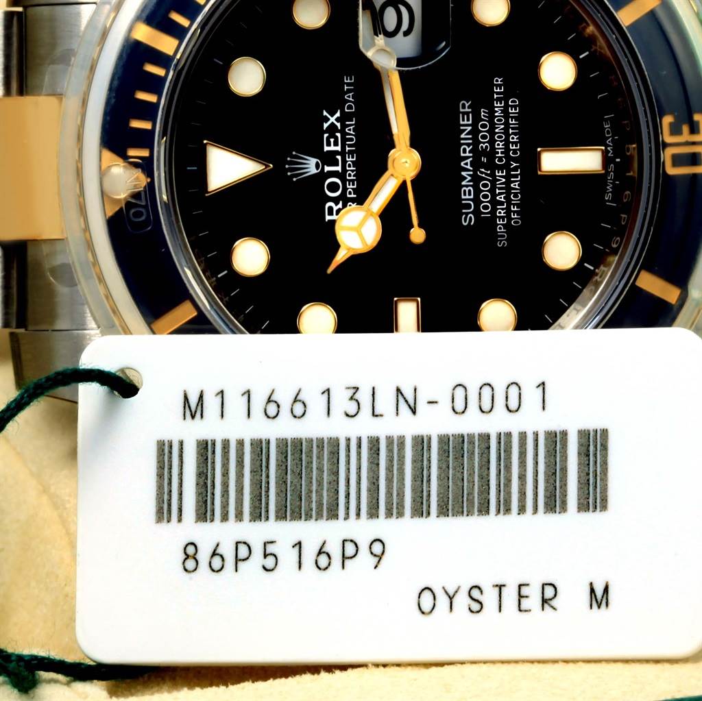 The image shows a close-up of the face of a Rolex Submariner 116613 Men
s Steel and Gold (two tone) Black Dial 116613 Men
s Steel and Gold (two tone) Black Dial watch, along with its tag displaying the model number.