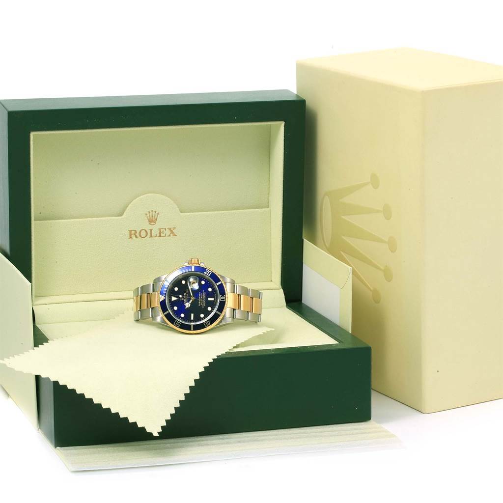 The Rolex Submariner 16613 Men's Steel and Gold (two tone) Blue Dial 16613 Men's Steel and Gold (two tone) Blue Dial watch is shown front-facing inside its green and beige display box, with a cleaning cloth.