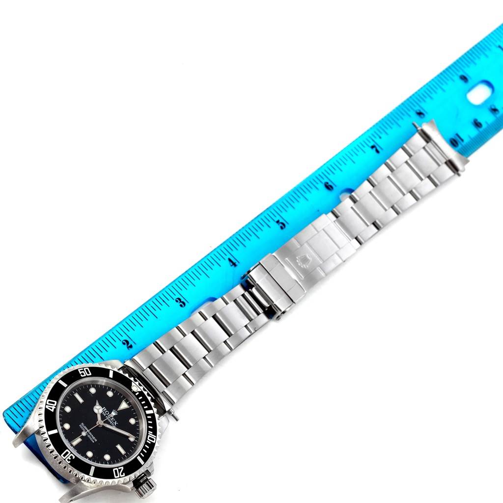 The image shows a Rolex Submariner 14060 Men's Stainless Steel Black Dial 14060 Men's Stainless Steel Black Dial laid flat against a blue ruler, highlighting its bracelet and clasp.