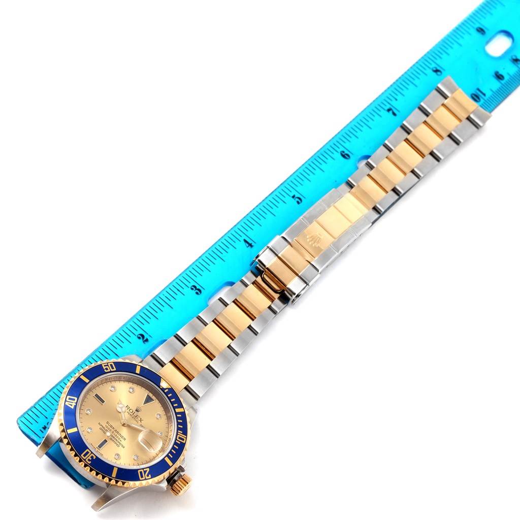 This image shows a Rolex Submariner 16613 Men's Steel and Gold (two tone) Champagne Dial 16613 Men's Steel and Gold (two tone) Champagne Dial watch at an oblique angle with the full length of its gold and silver bracelet next to a ruler.