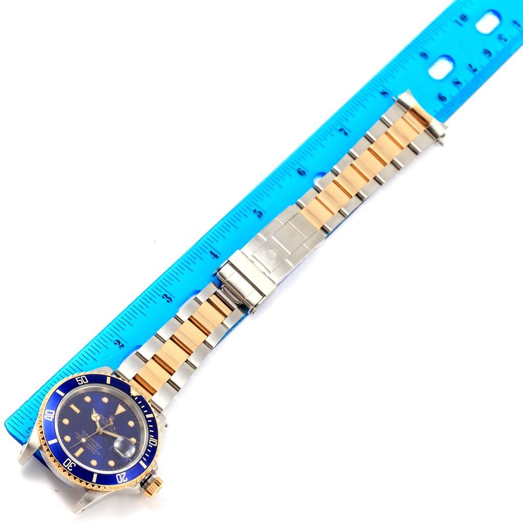 The Rolex Submariner 16613 Men's Steel and Gold (two tone) Blue Dial 16613 Men's Steel and Gold (two tone) Blue Dial watch is shown from a top angle, displaying its face, bezel, bracelet, and clasp next to a ruler.